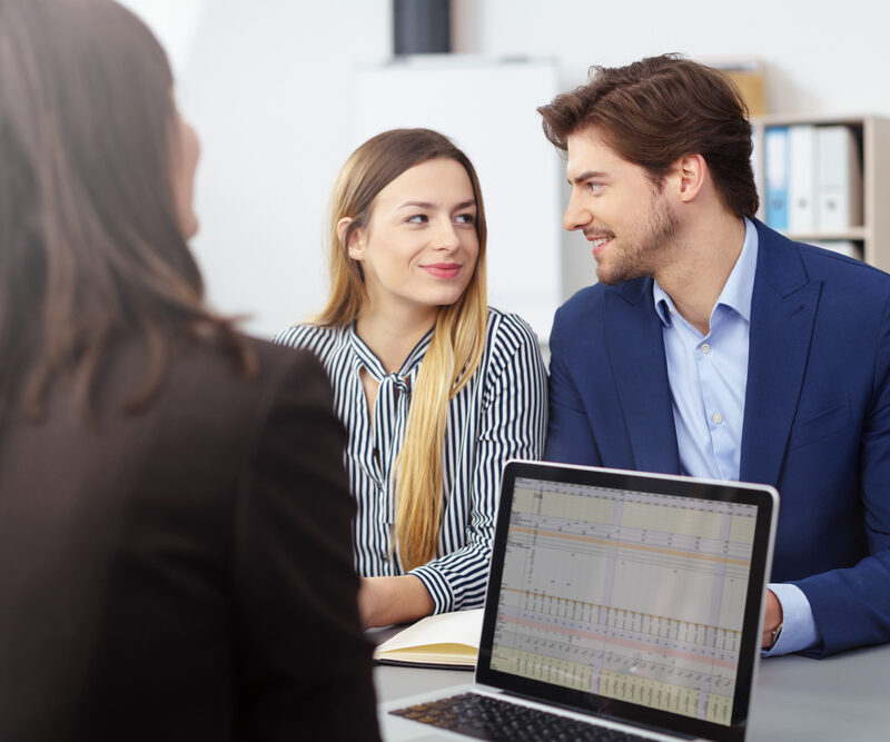 Young married couple in a meeting with a broker or agent sitting looking at each other smiling as they reach a decision